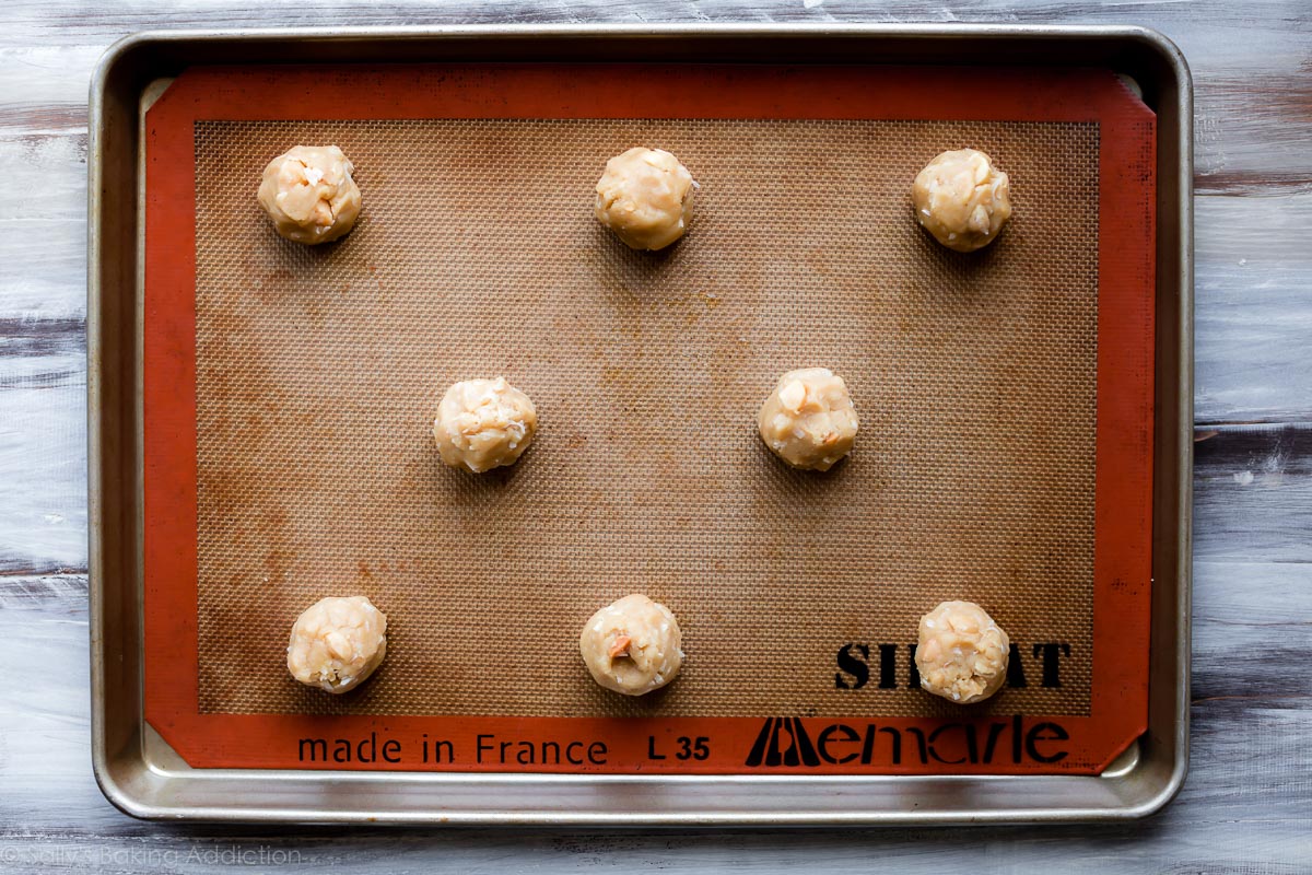 Coconut macadamia nut cookie dough rolled into balls on a Silpat lined baking sheet before baking