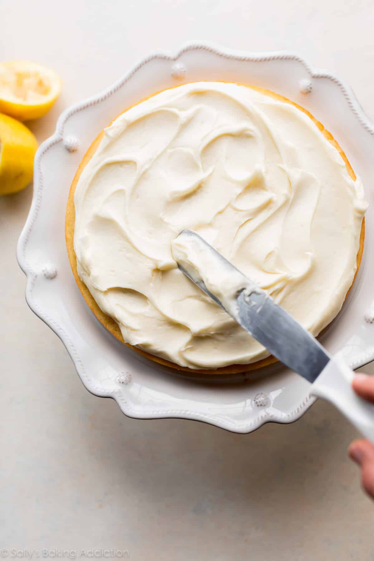 spreading frosting onto lemon cake on a white cake stand