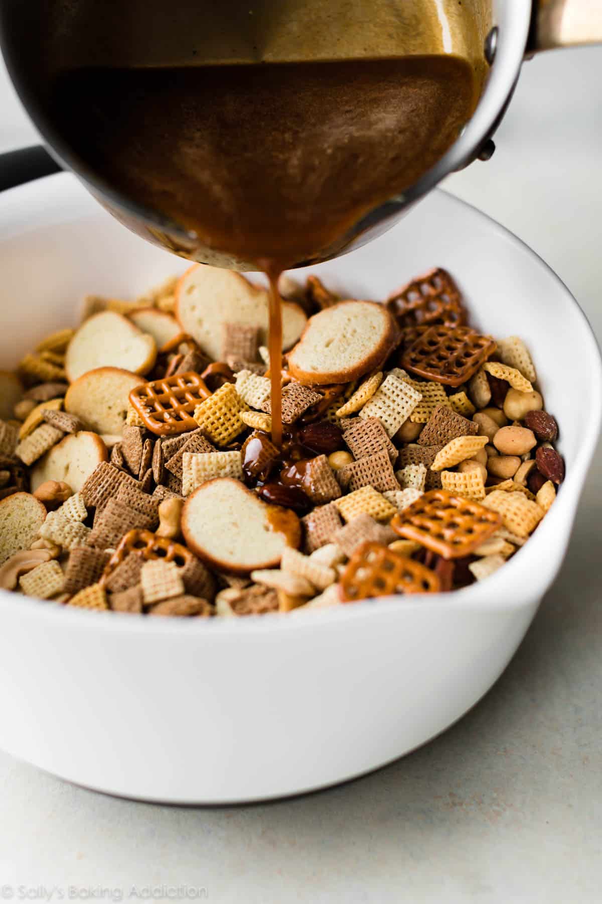 pouring Chex mix sauce into a bowl of dry ingredients