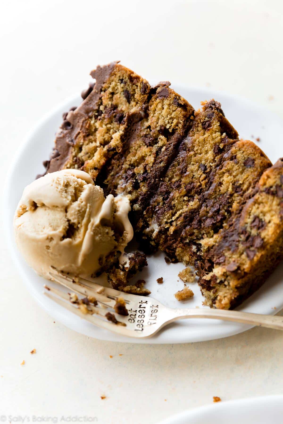 slice of chocolate chip cookie layer cake on a white plate with a scoop of ice cream