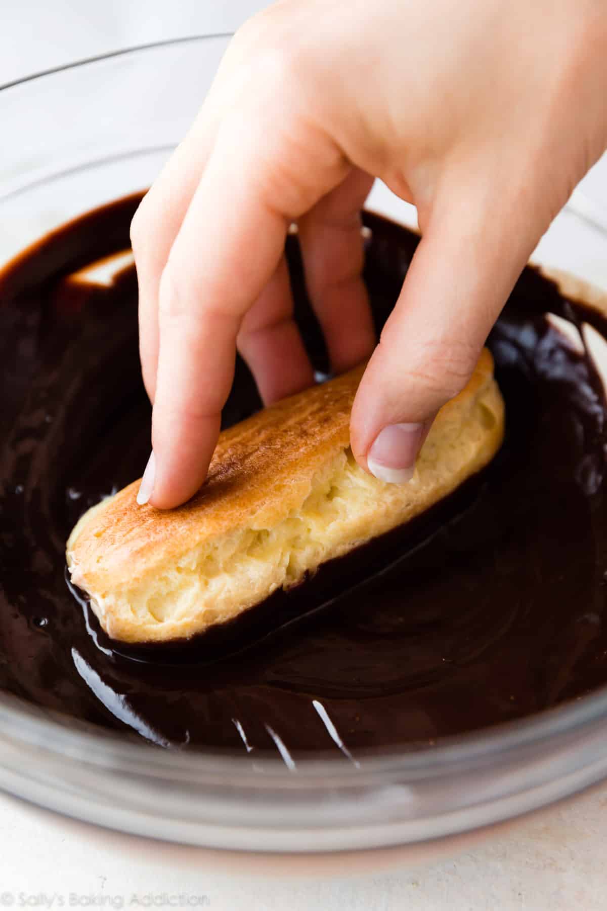 Dipping homemade eclairs into a bowl of chocolate ganache topping