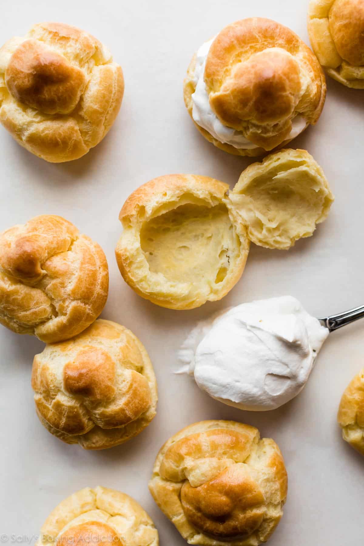 spooning whipped cream filling into baked cream puffs