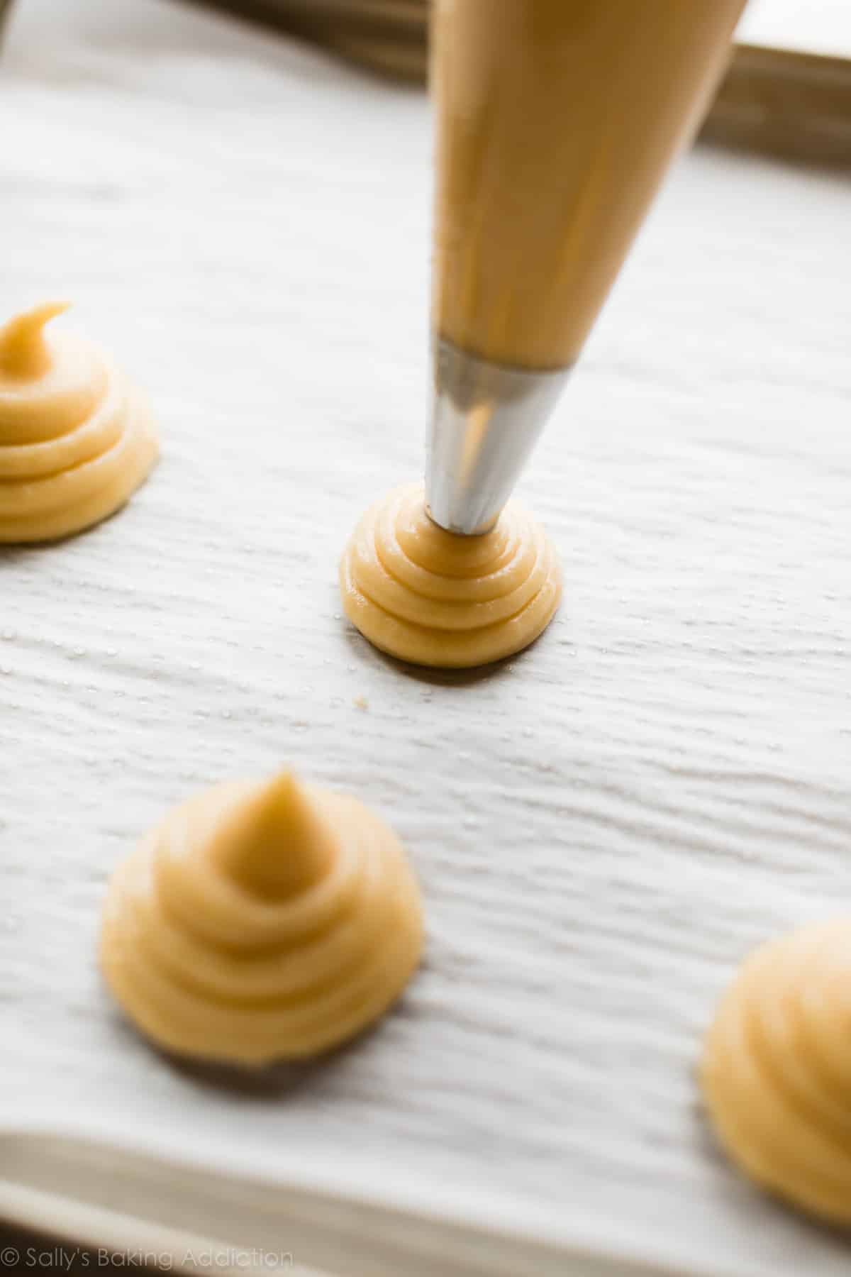 piping choux pastry onto a baking sheet lined with parchment paper