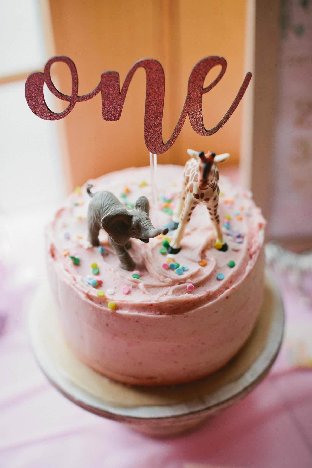 pink 1st birthday cake with cake topper that says one