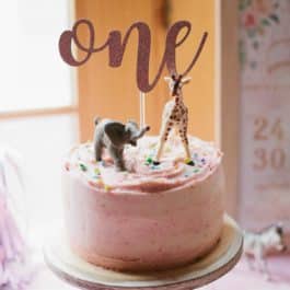 pink 1st birthday cake on a cake stand with safari animal cake toppers