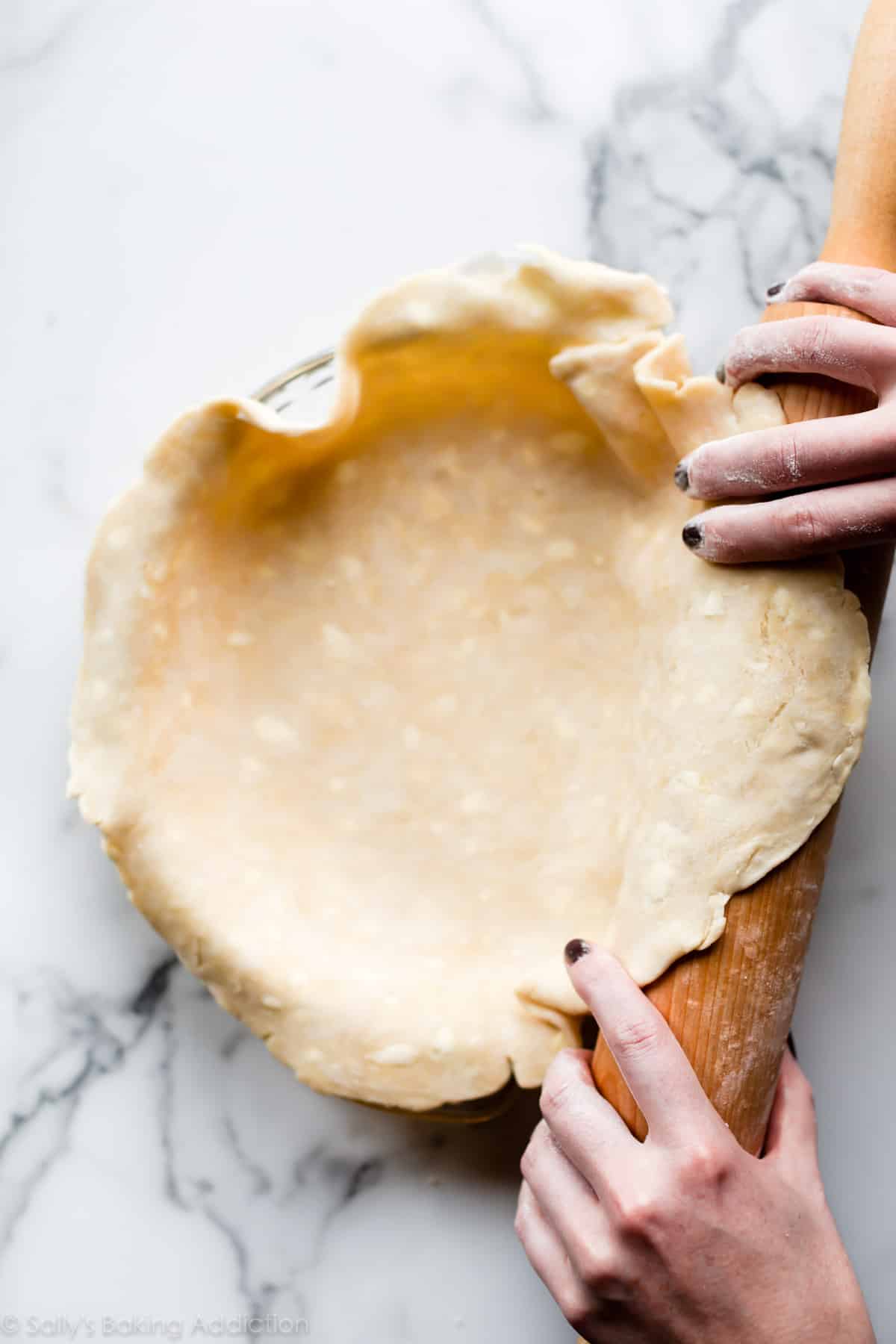 pie dough rolled out into glass pie dish with wood rolling pin