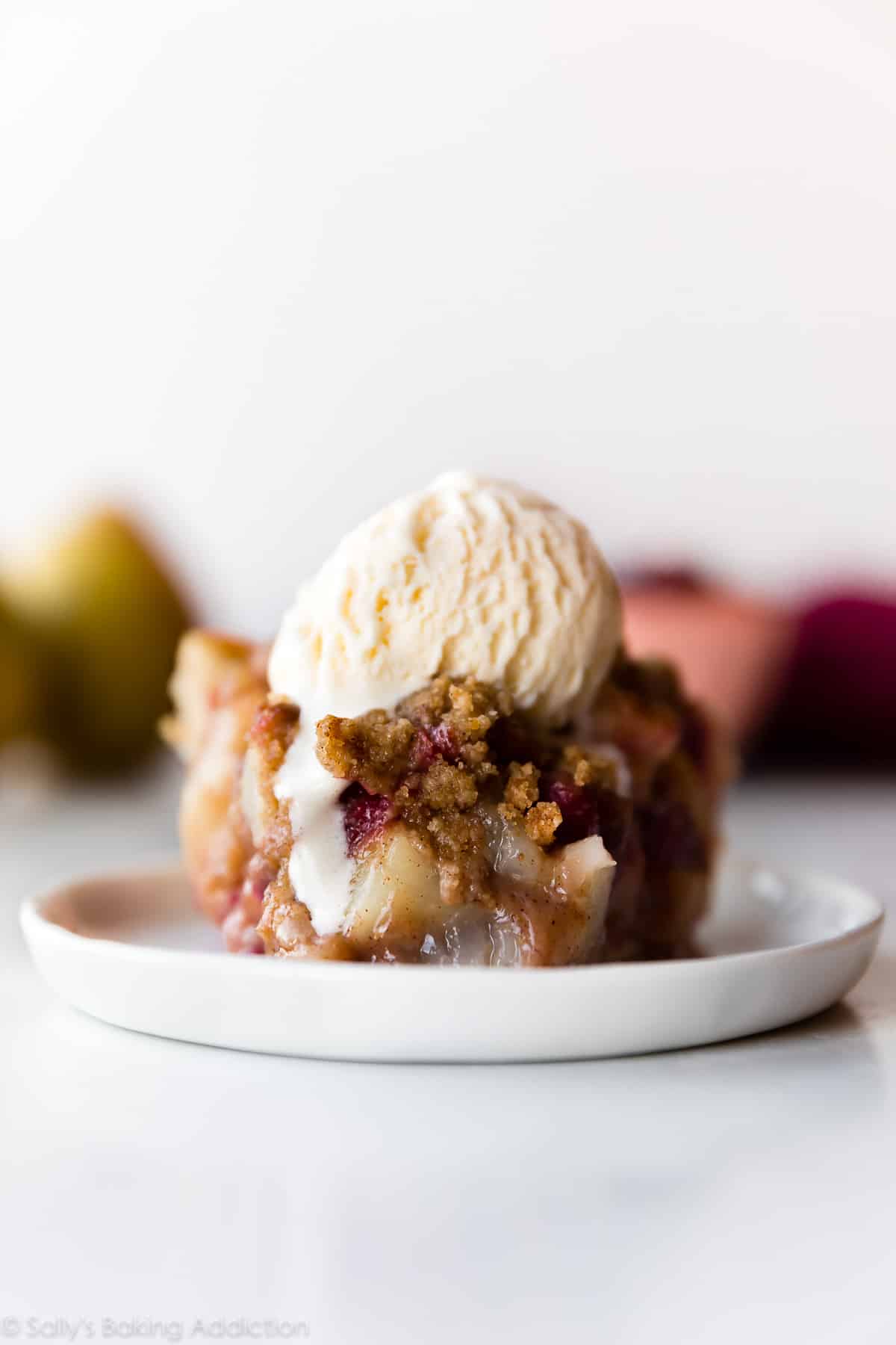 slice of cranberry pear crumble pie with a scoop of ice cream on a white plate