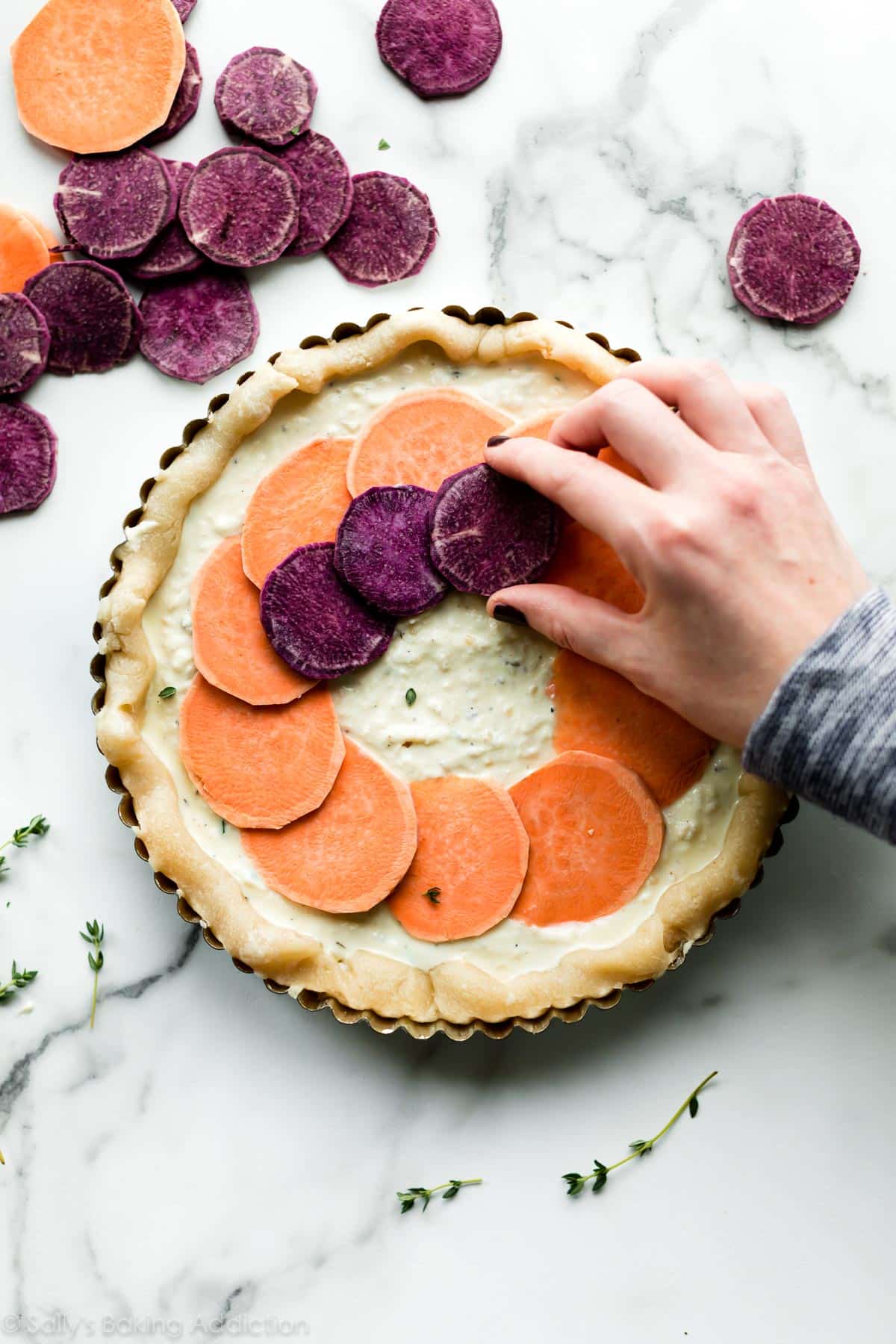 hand placing vegetable toppings onto vegetable and cheese tart