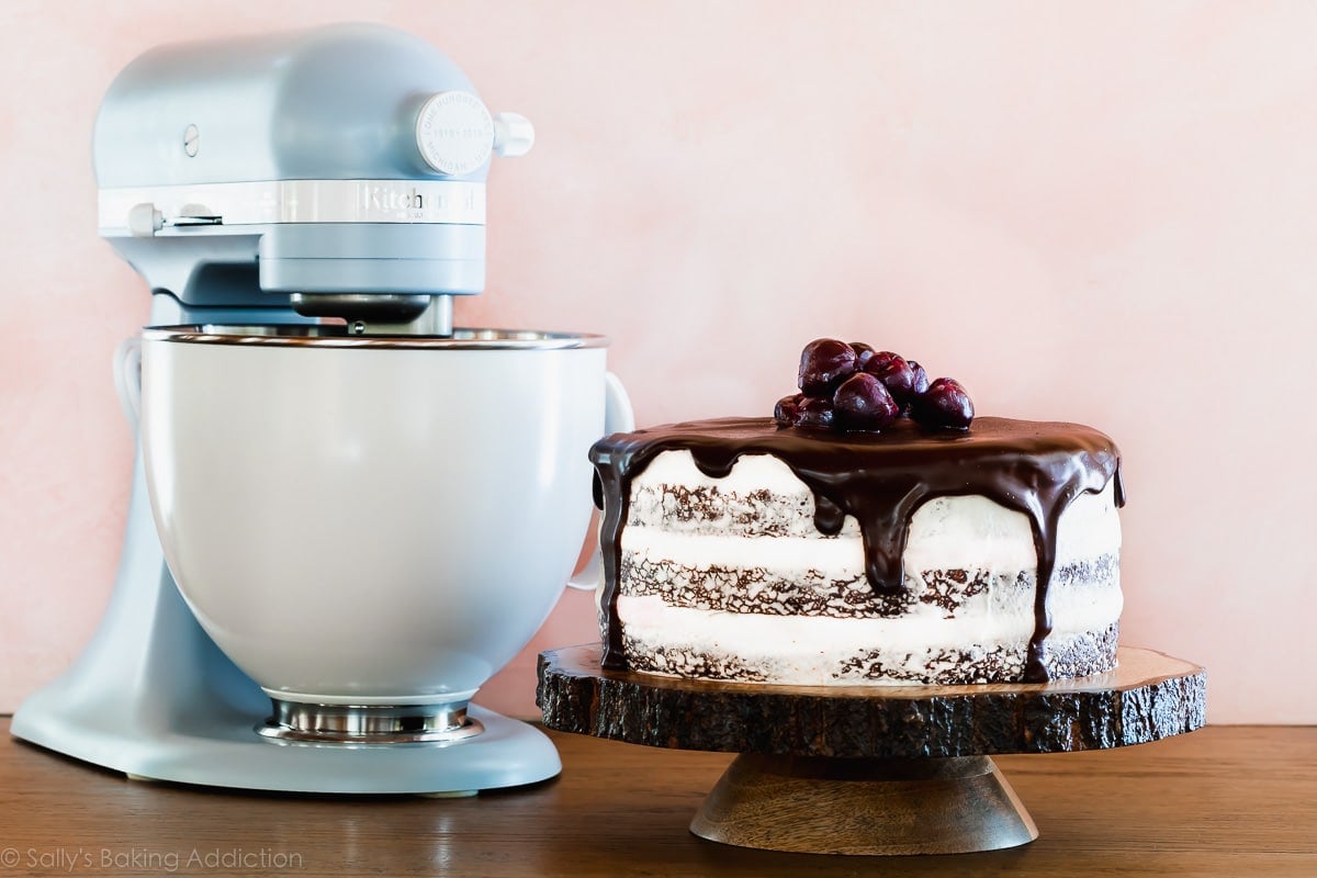 Black Forest Cake on a wood slice cake stand with a KitchenAid stand mixer in the background
