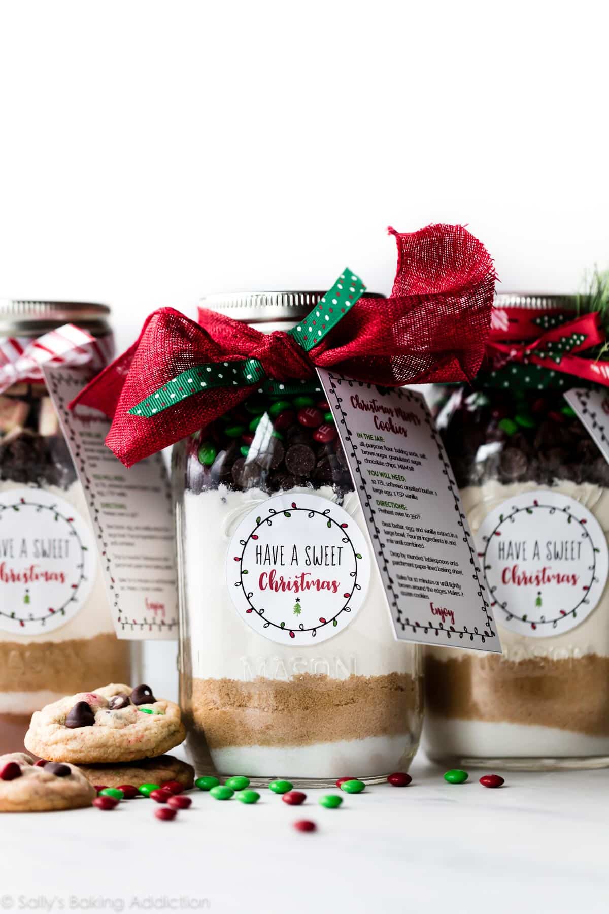 glass jars with ingredients for cookies decorated with ribbon and a recipe card