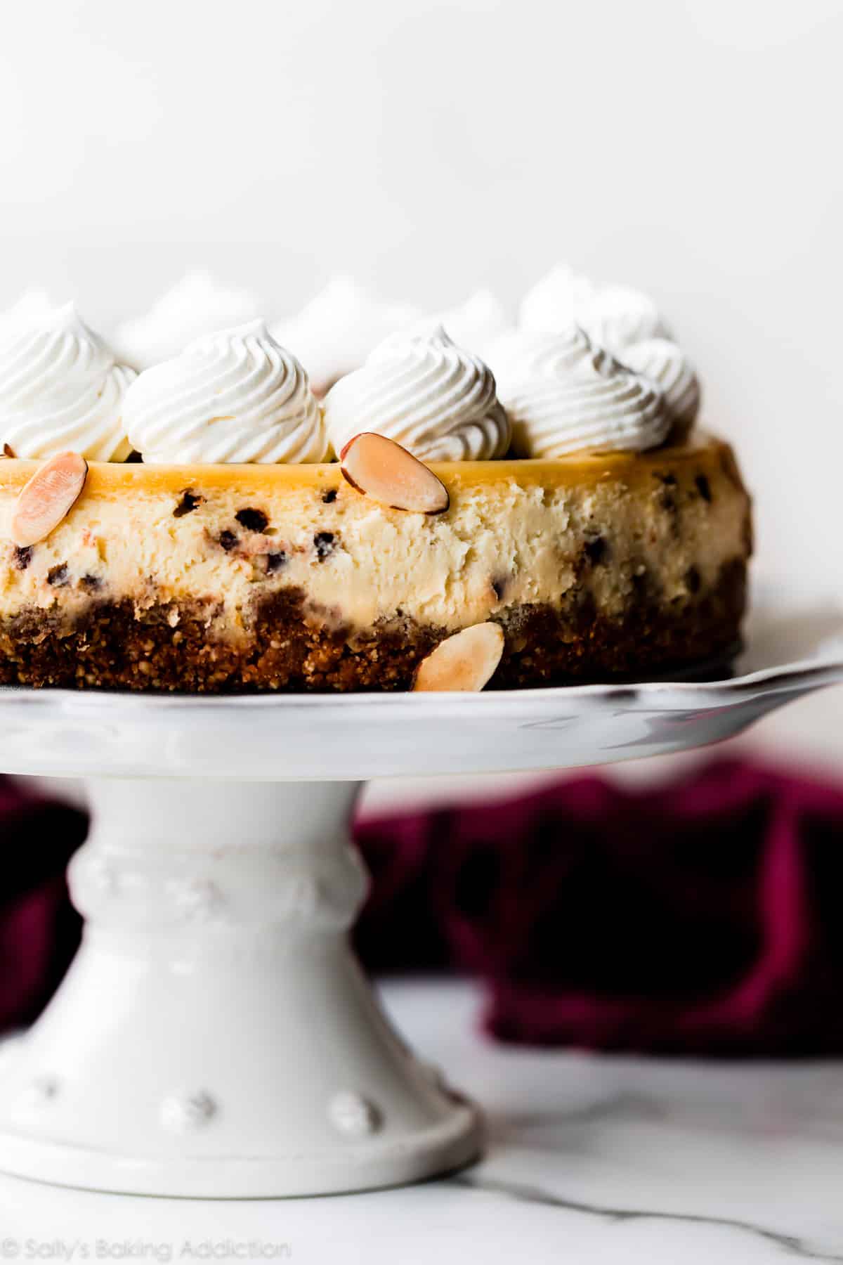 Amaretto chocolate chip cheesecake with whipped cream on a white cake stand