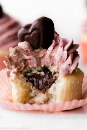 close-up photo of Valentine's Day cupcake with a bite taken out topped with strawberry Nutella frosting and chocolate heart candy.