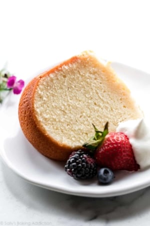 slice of cream cheese pound cake on a white plate with whipped cream and berries