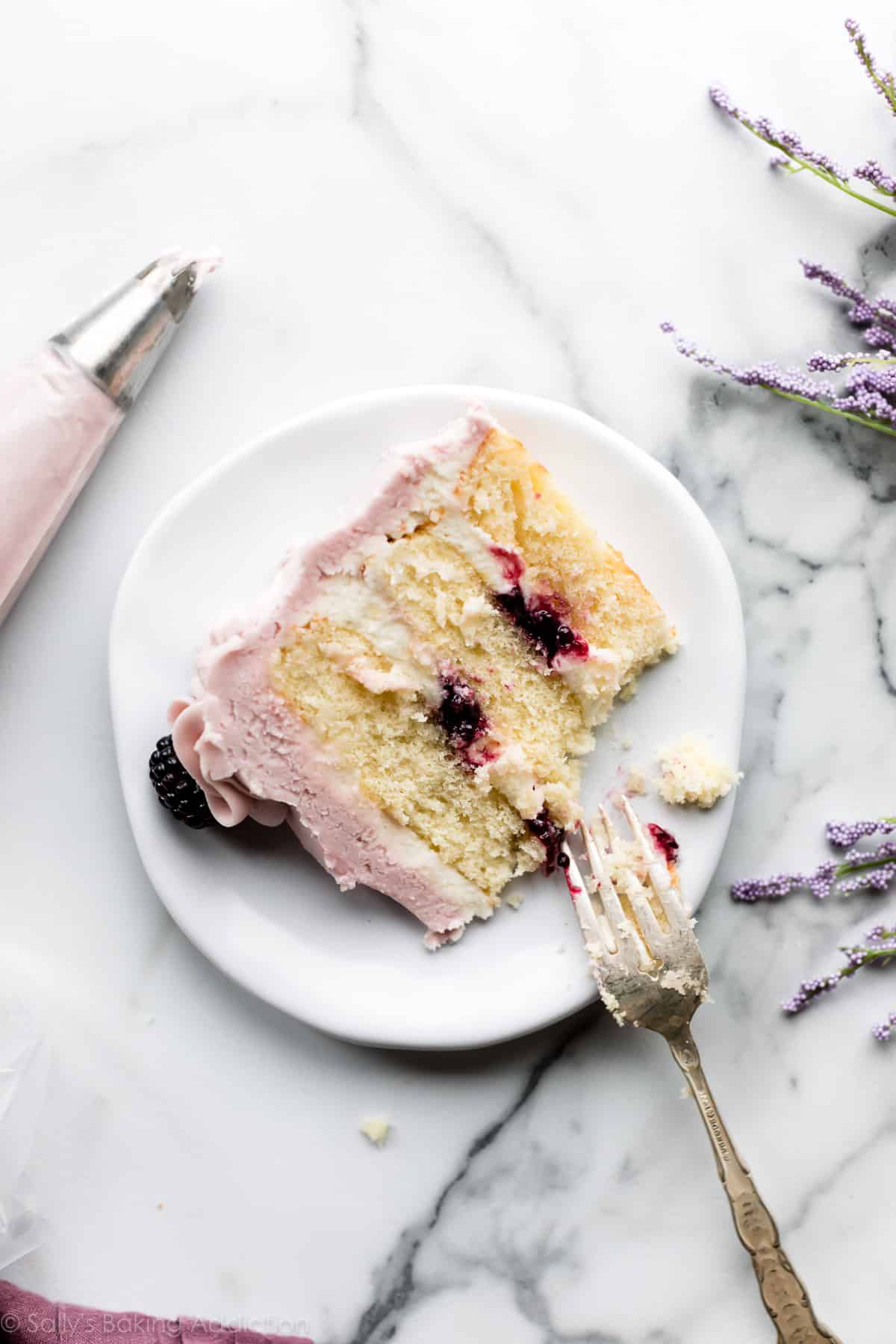 Slice of lavender butter cake with purple frosting and blackberry jam on a white plate