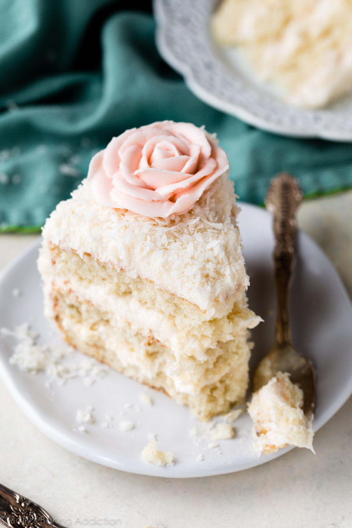 Slice of coconut cake with buttercream flower on white plate