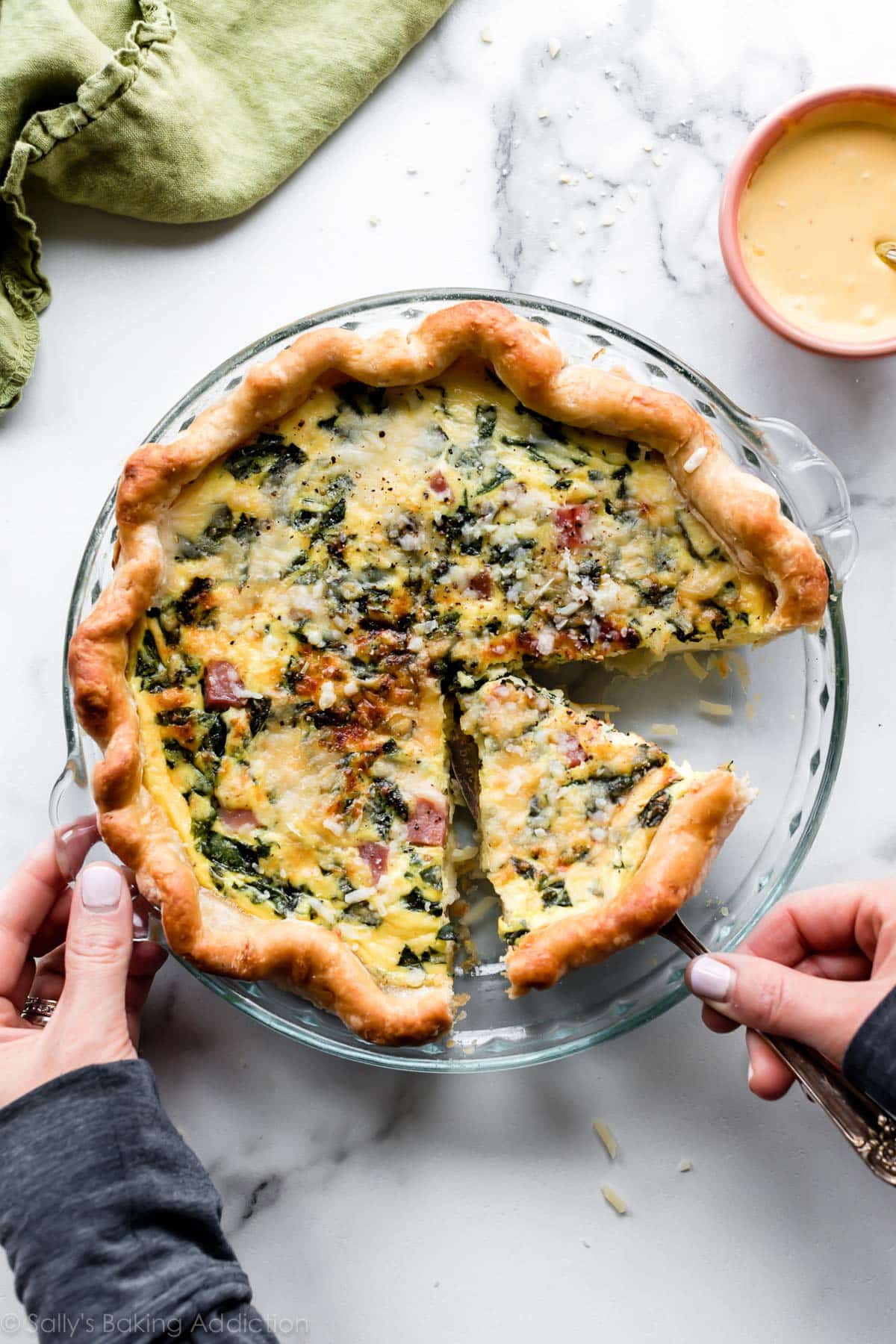 Quiche with spinach in a glass pie dish with a slice on a pie server