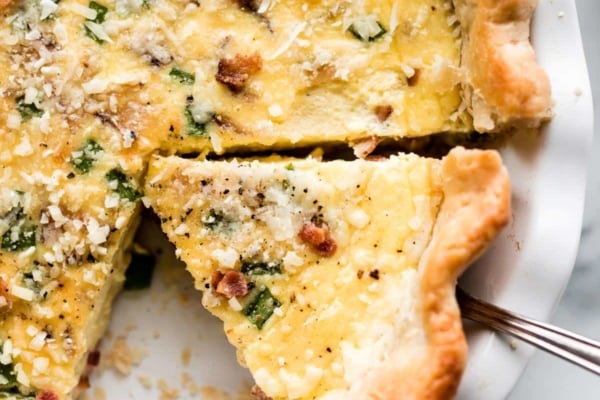 Quiche with bacon in a white pie dish with a slice being removed