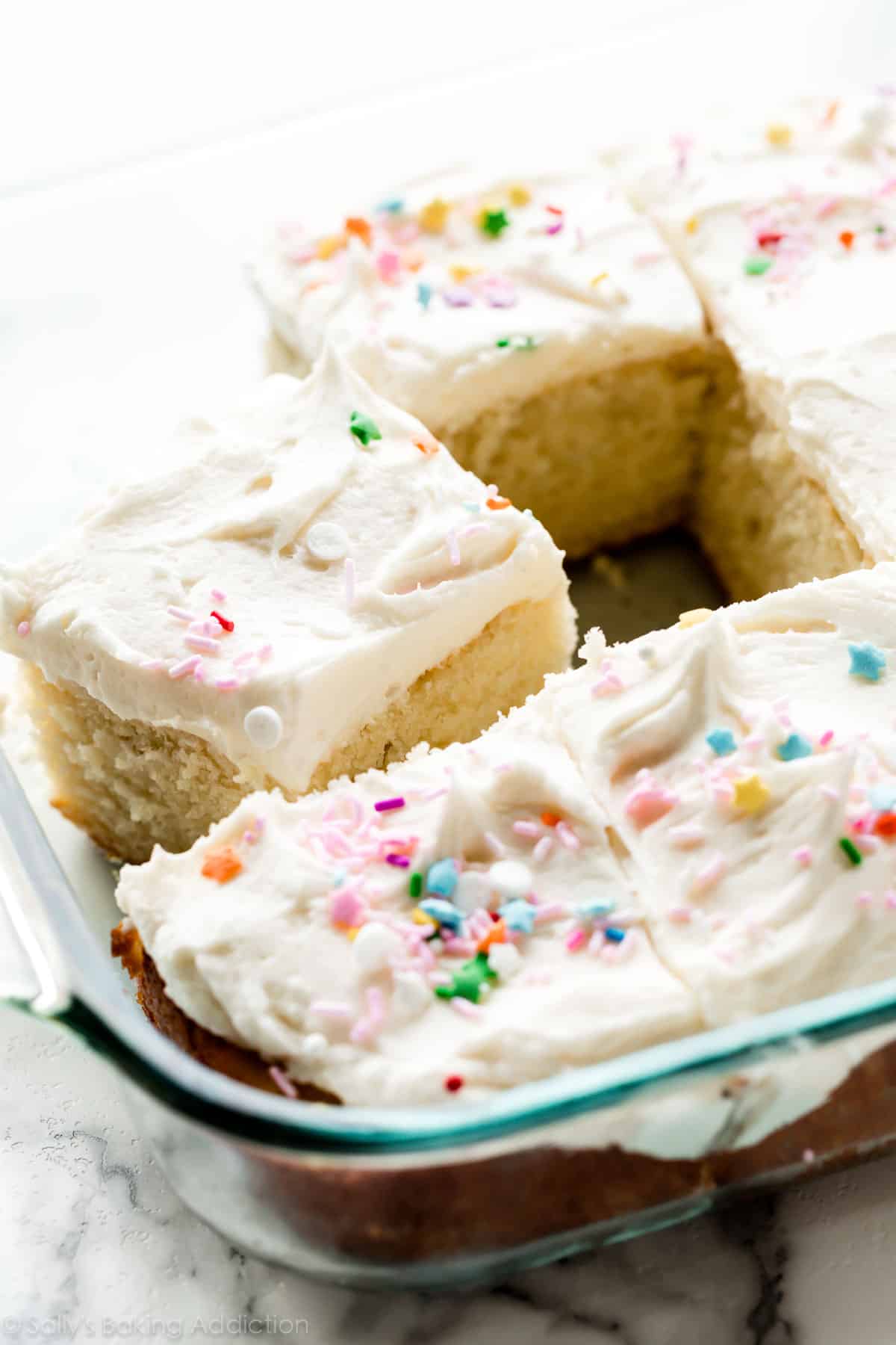 sliced vanilla sheet cake in a glass baking pan topped with sprinkles