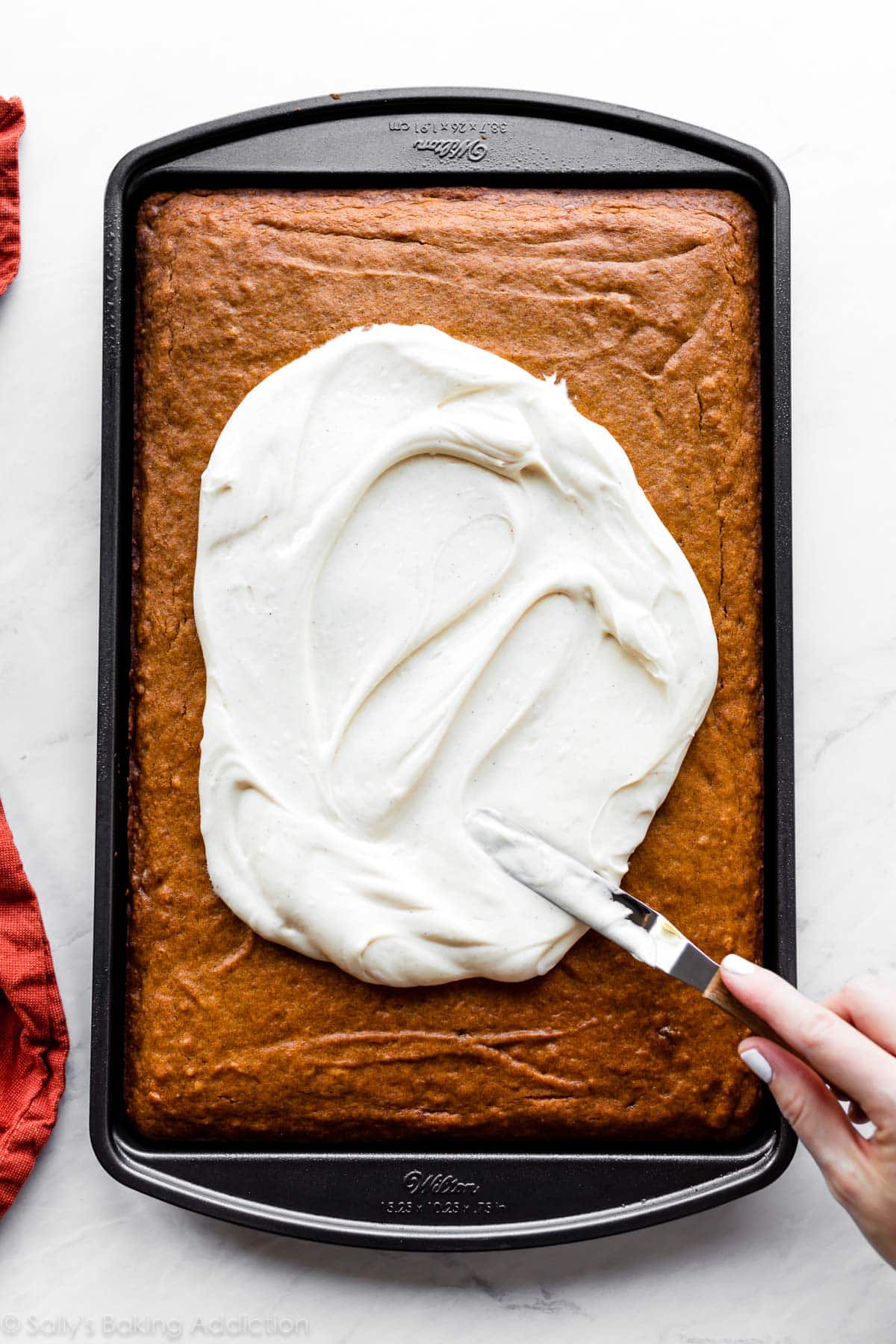 spreading cream cheese frosting on a sheet pan of pumpkin bars