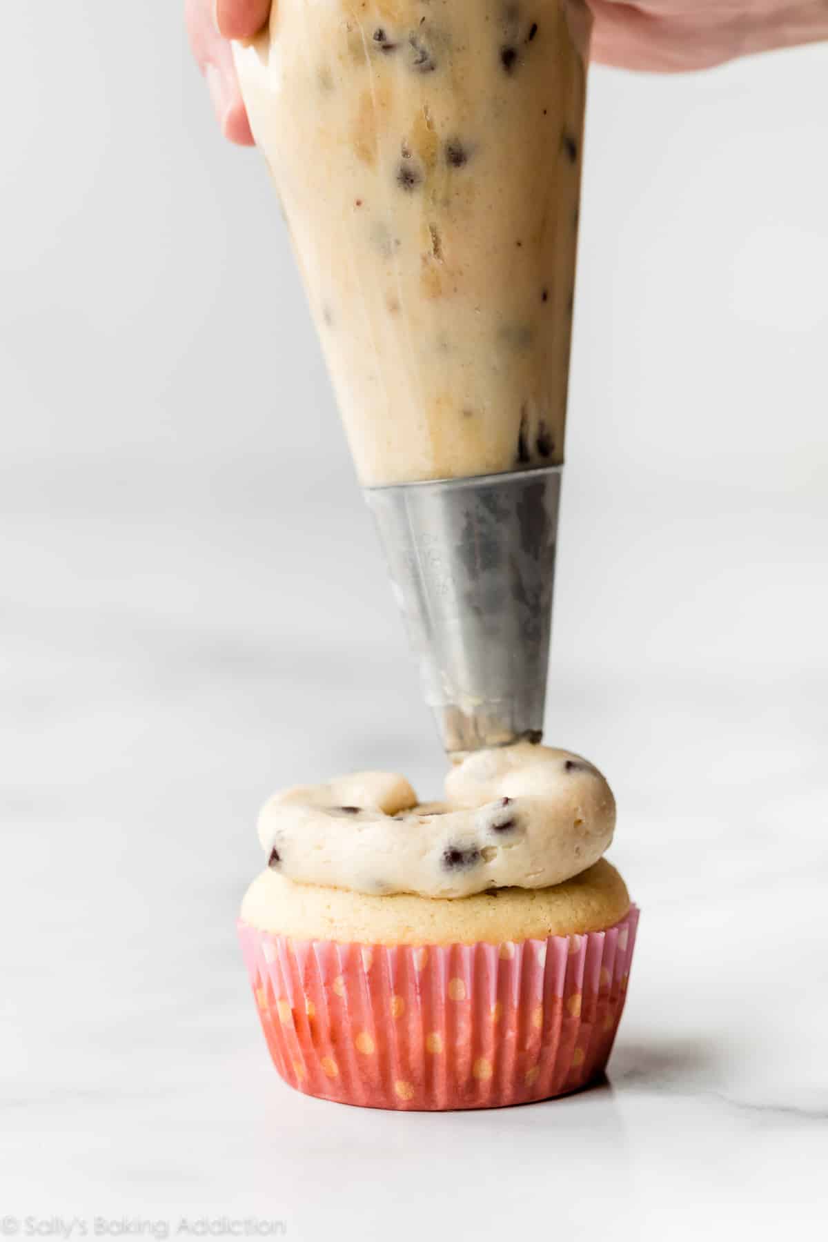 piping cookie dough frosting on a cupcake