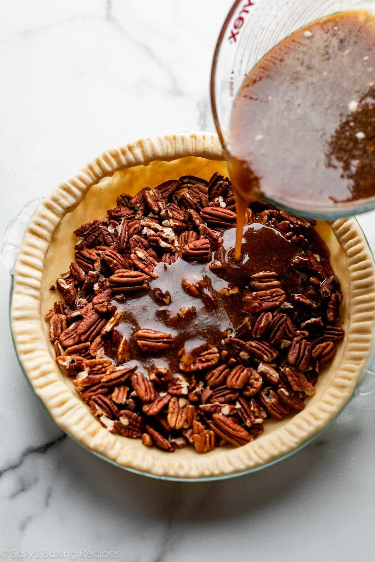 pouring syrup over pecans in pie dough with crimped edges.