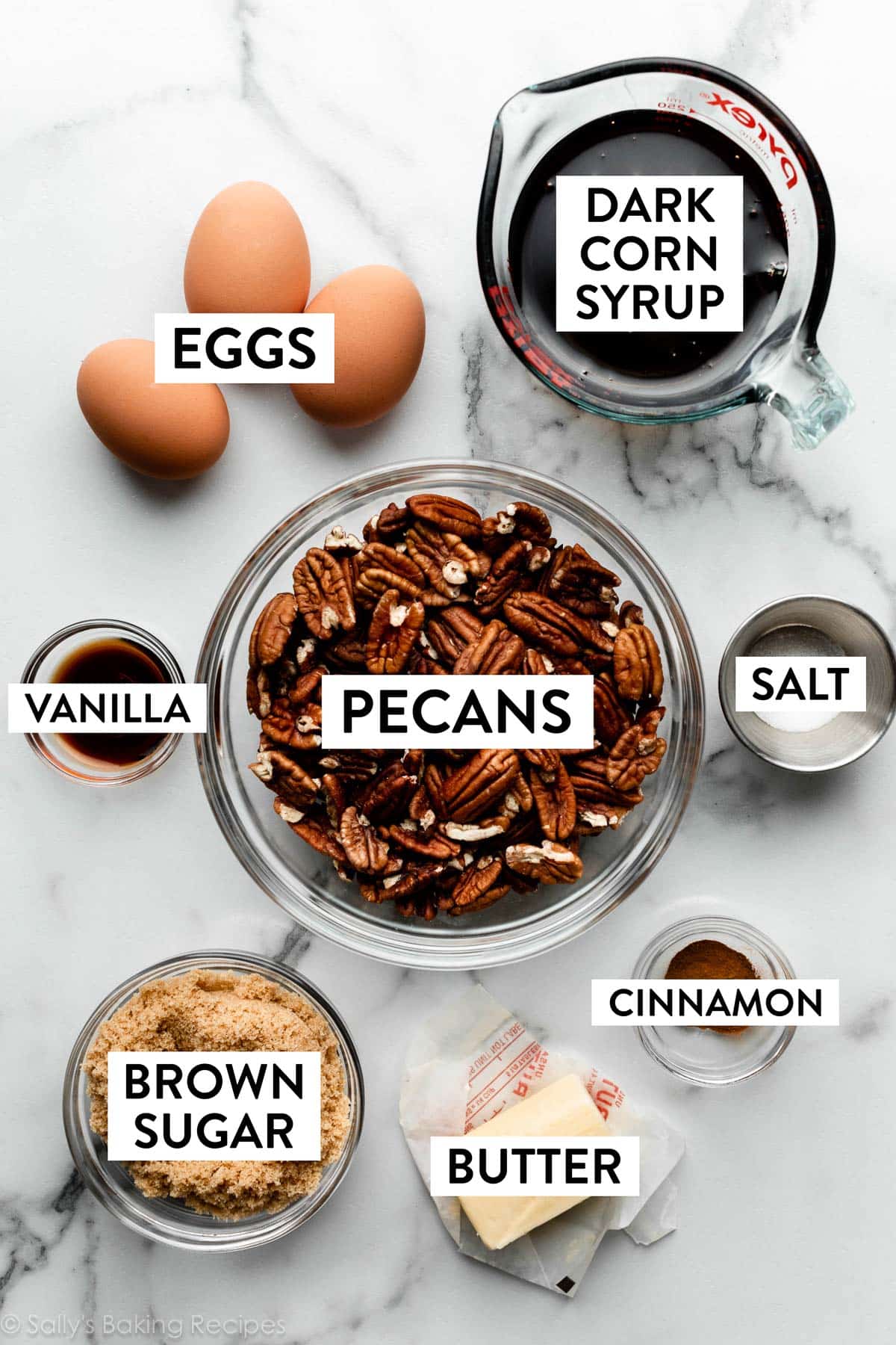 measured ingredients on marble counter including dark corn syrup, eggs, pecans, brown sugar, and butter.