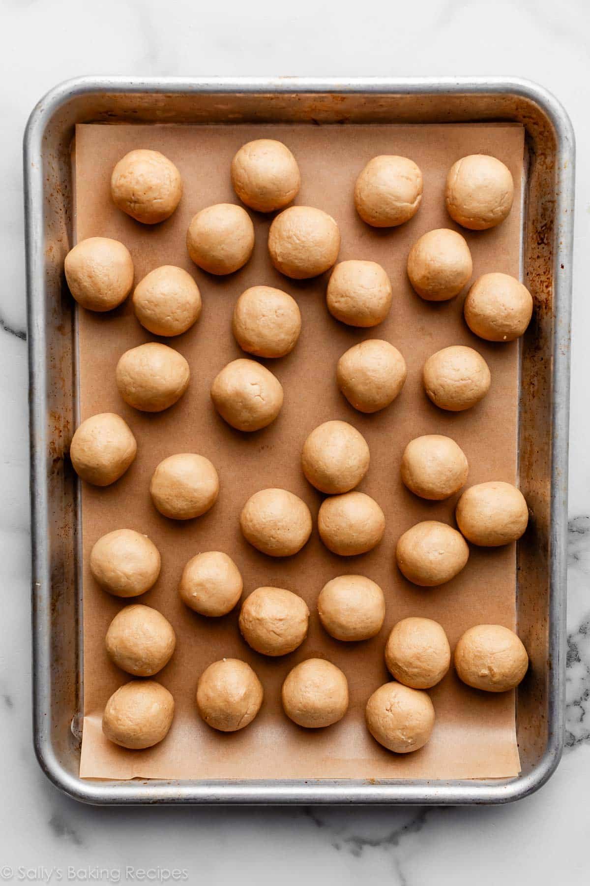 peanut butter dough mixture rolled into balls on lined baking sheet.