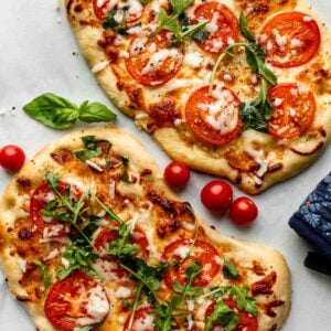 homemade flatbread pizza with mozzarella cheese, tomatoes, and arugula on top.