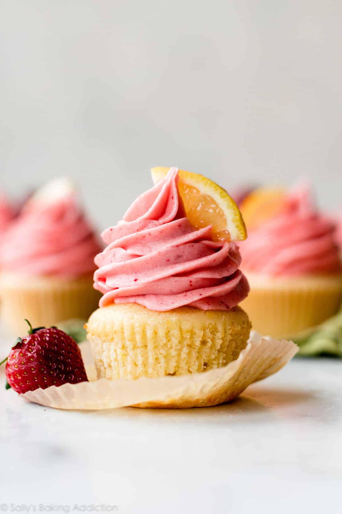 unwrapped lemon cupcake with strawberry frosting and a lemon slice on top