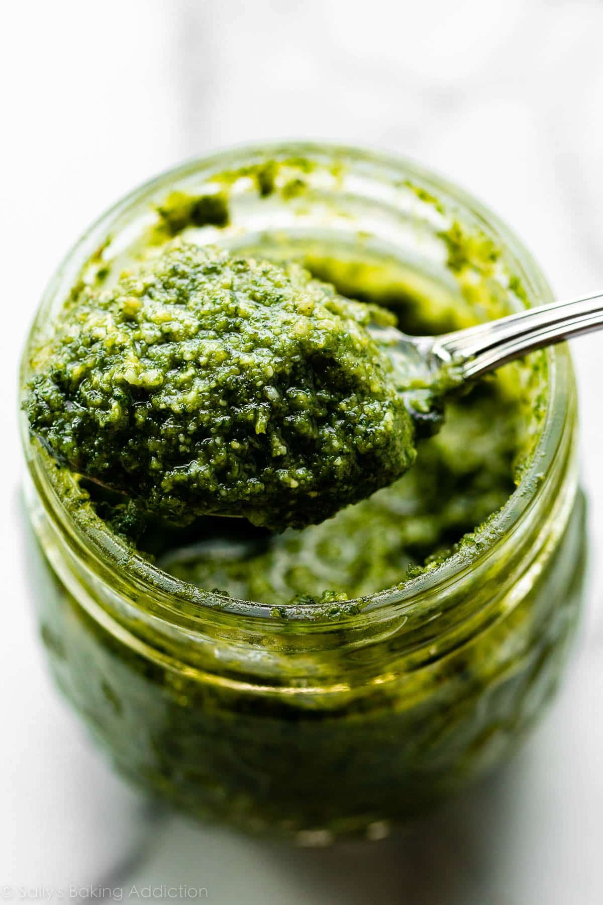 spoonful of homemade basil pesto coming out of a jar.