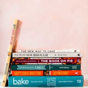 stack of baking cookbooks with a pink background