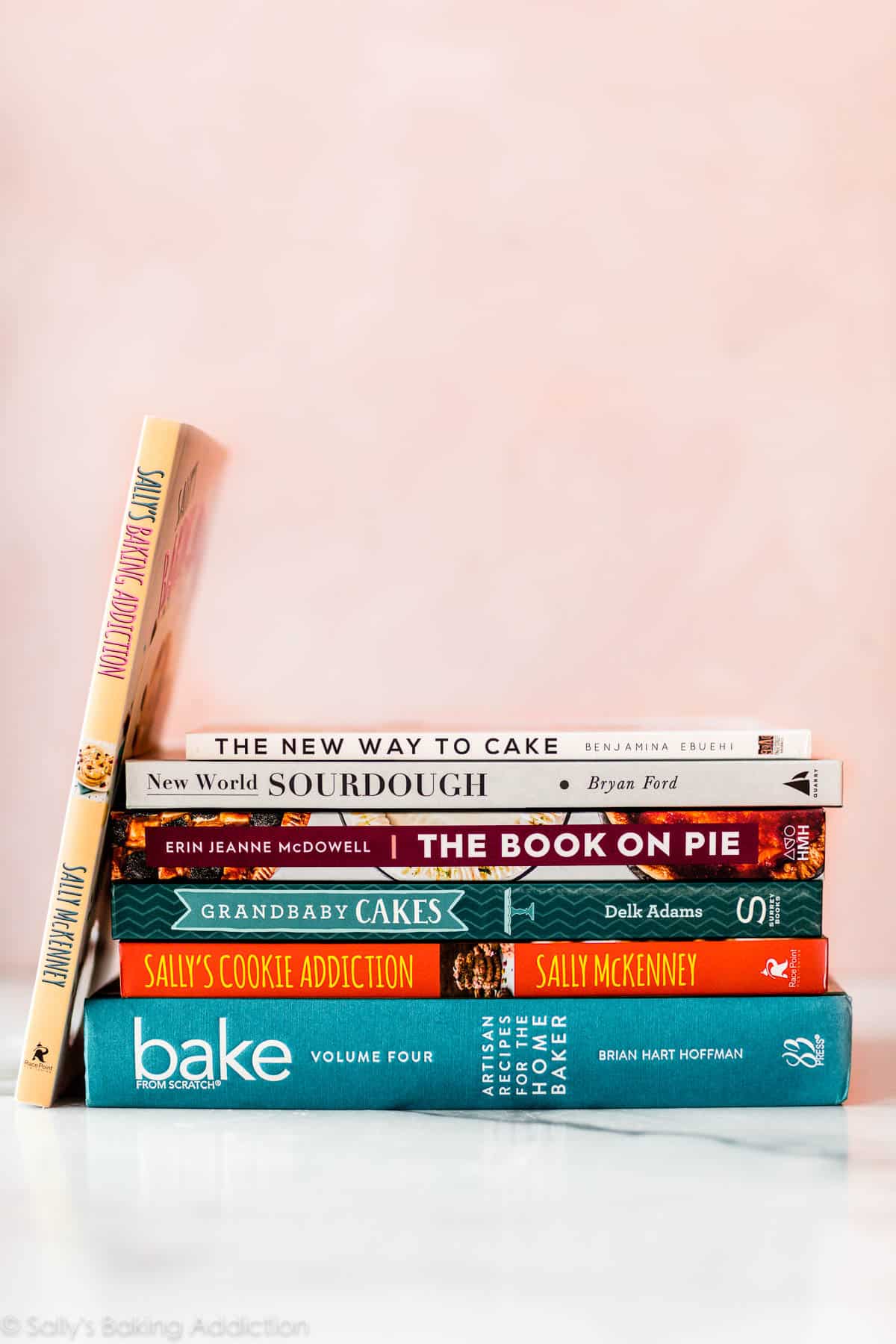 stack of baking cookbooks with a pink background