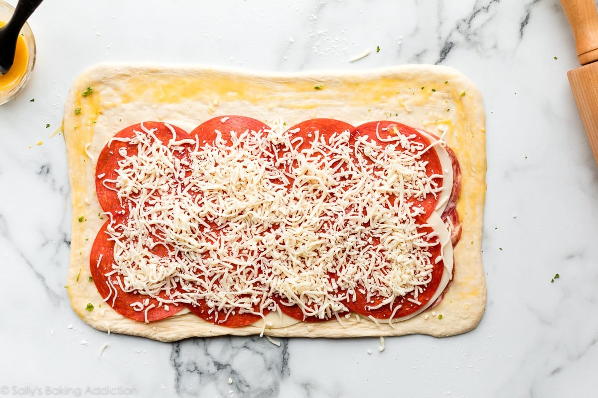 rectangle shape of dough with deli meats and cheese arranged on top