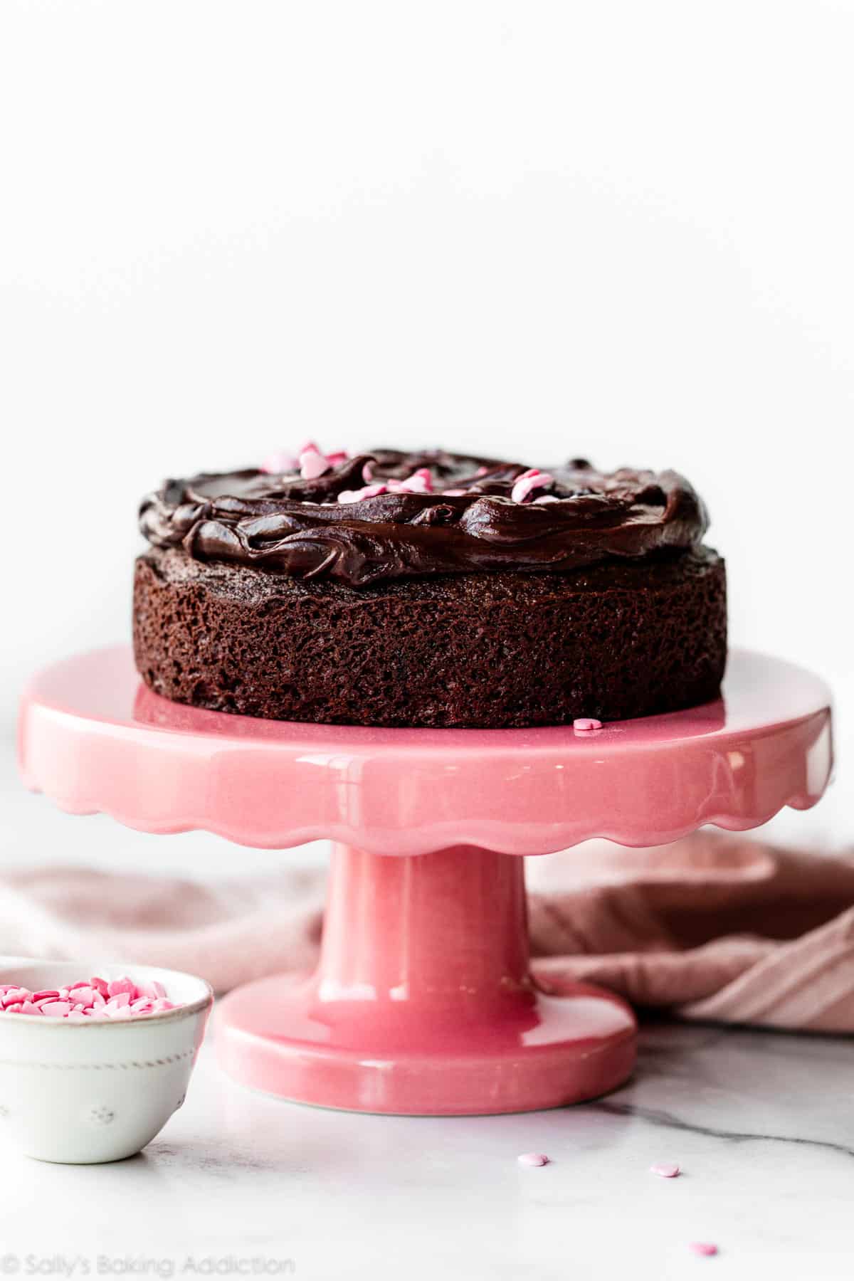 6 inch chocolate cake with chocolate ganache on top sitting on a pink cake stand