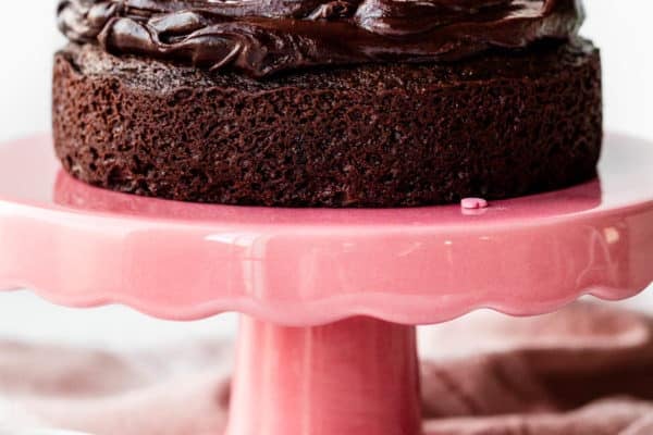 6 inch chocolate cake with chocolate ganache on top sitting on a pink cake stand.