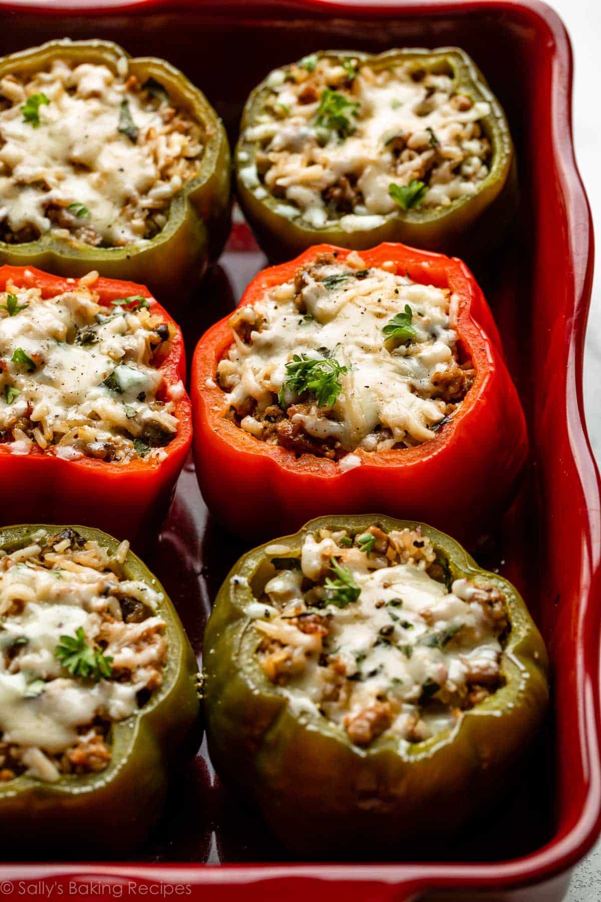 sausage and rice stuffed peppers with chopped parsley on top in red casserole dish.