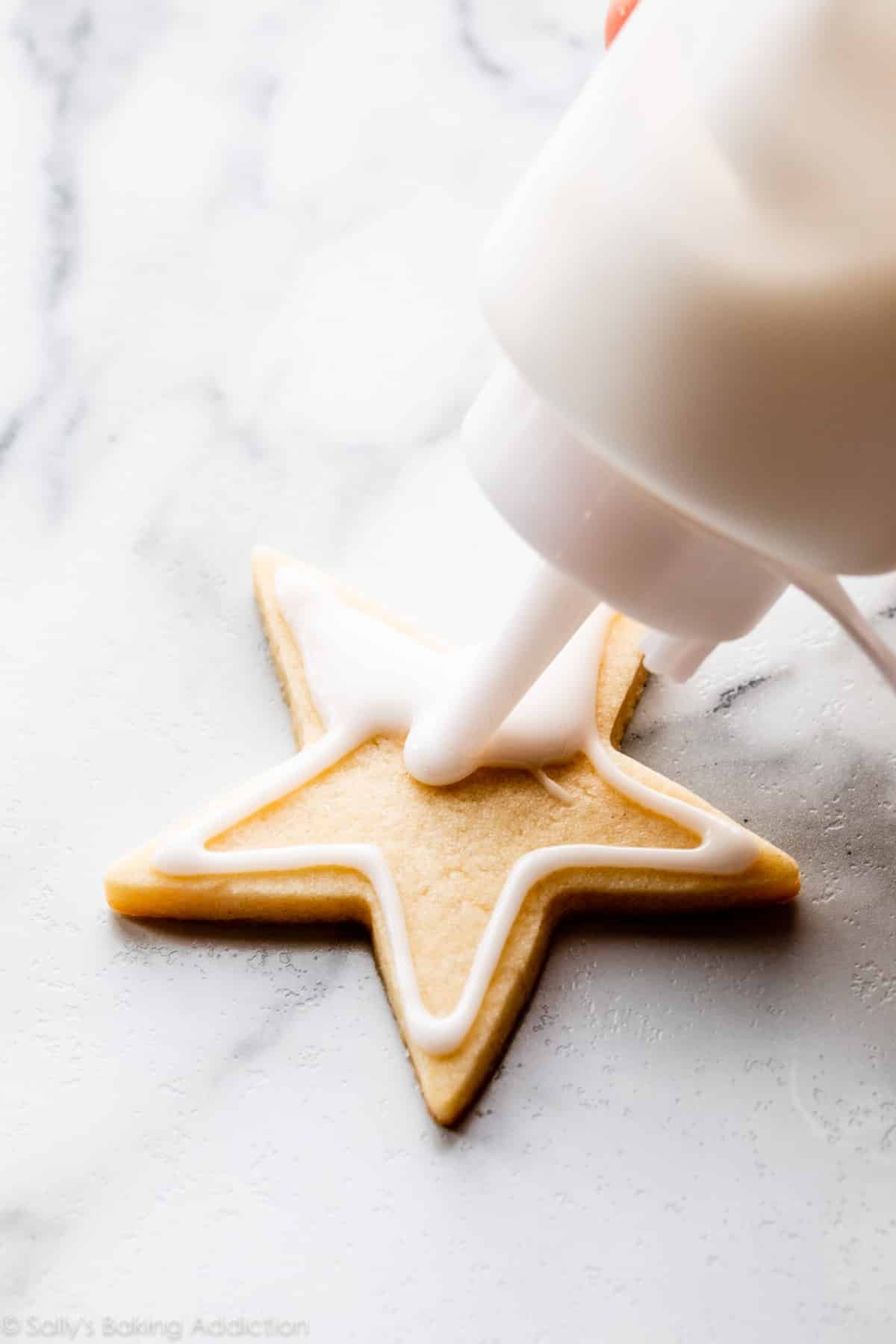 decorating a sugar cookie with white icing using a squeeze bottle