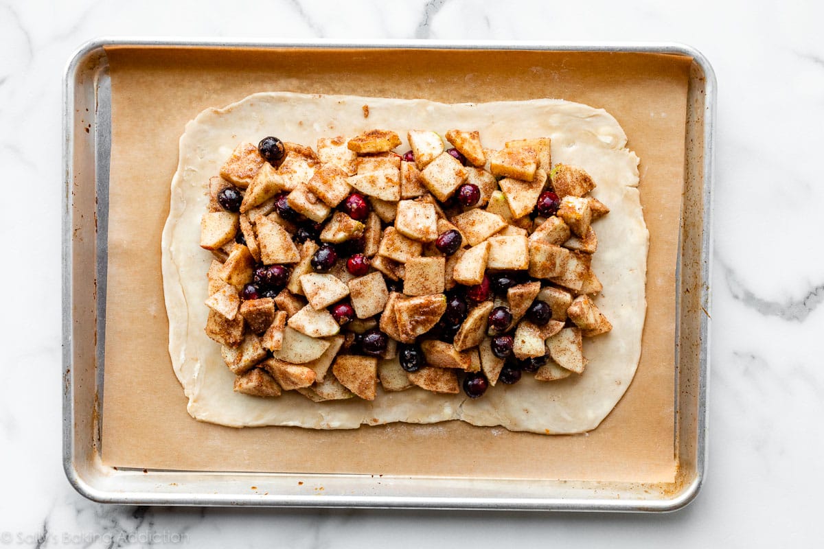 pie dough rolled out into a rectangle with apple cranberry filling on top