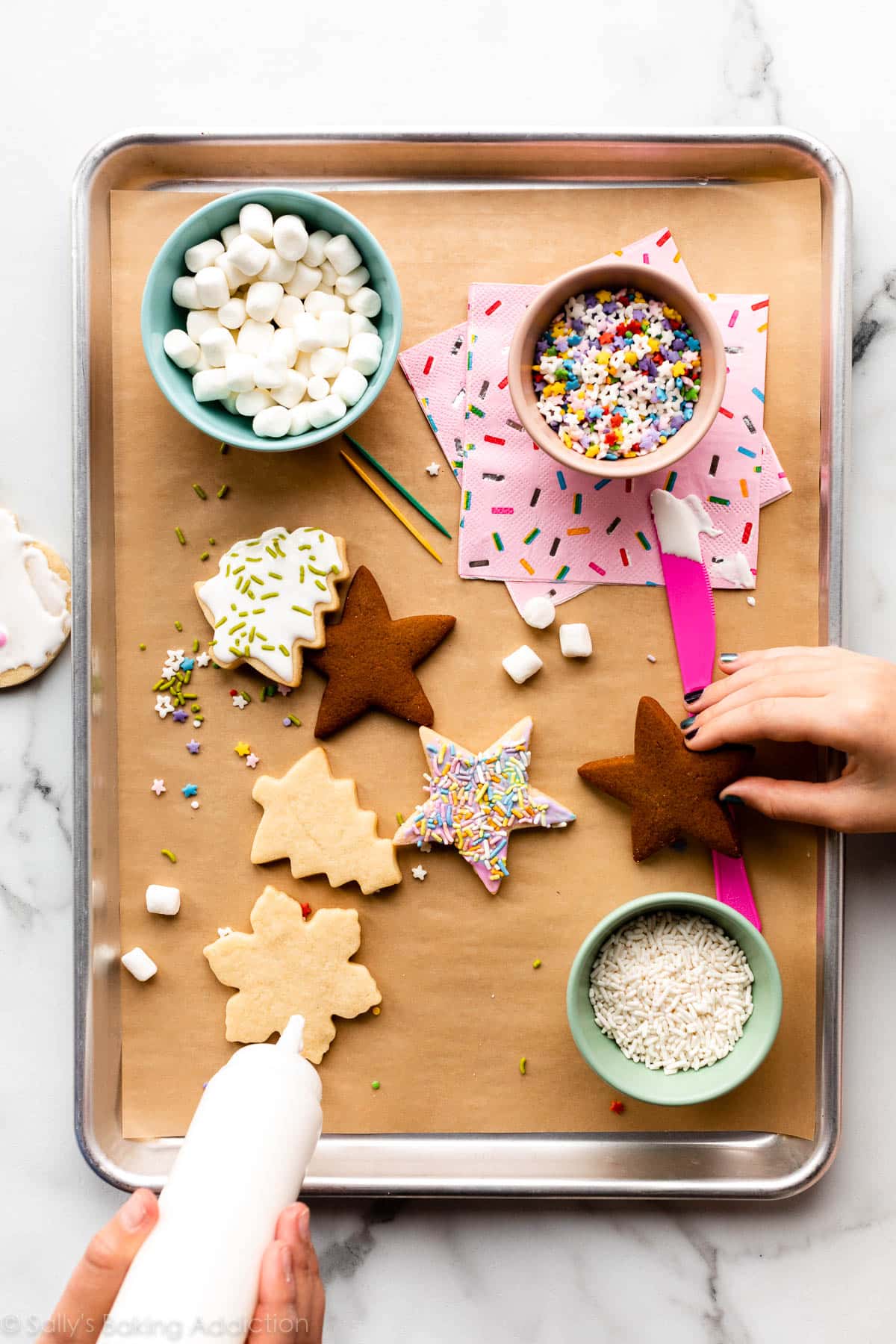 cookie decorating station with cookies, icing, and sprinkles on a lined baking sheet