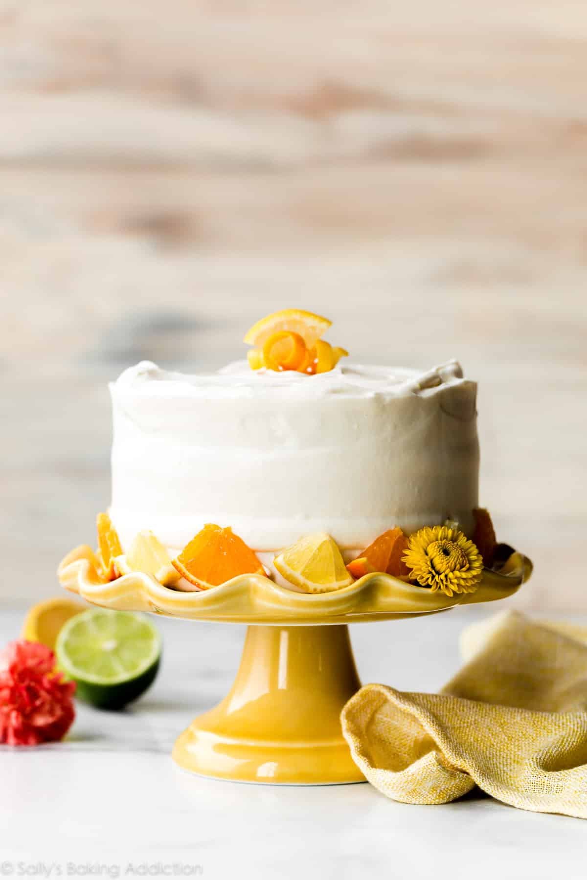 6 inch cake with whipped frosting and citrus fruits sitting on a yellow cake stand