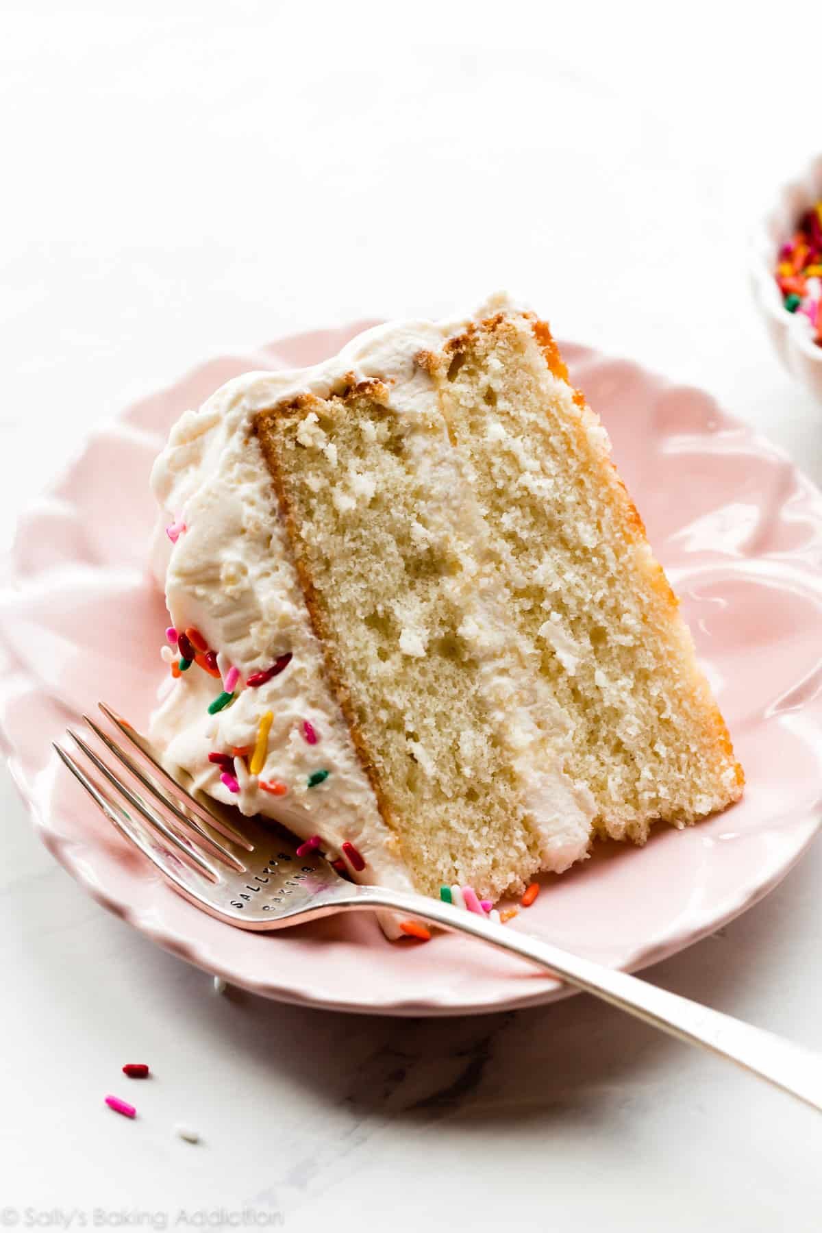 slice of white two layer cake with whipped frosting on pink plate