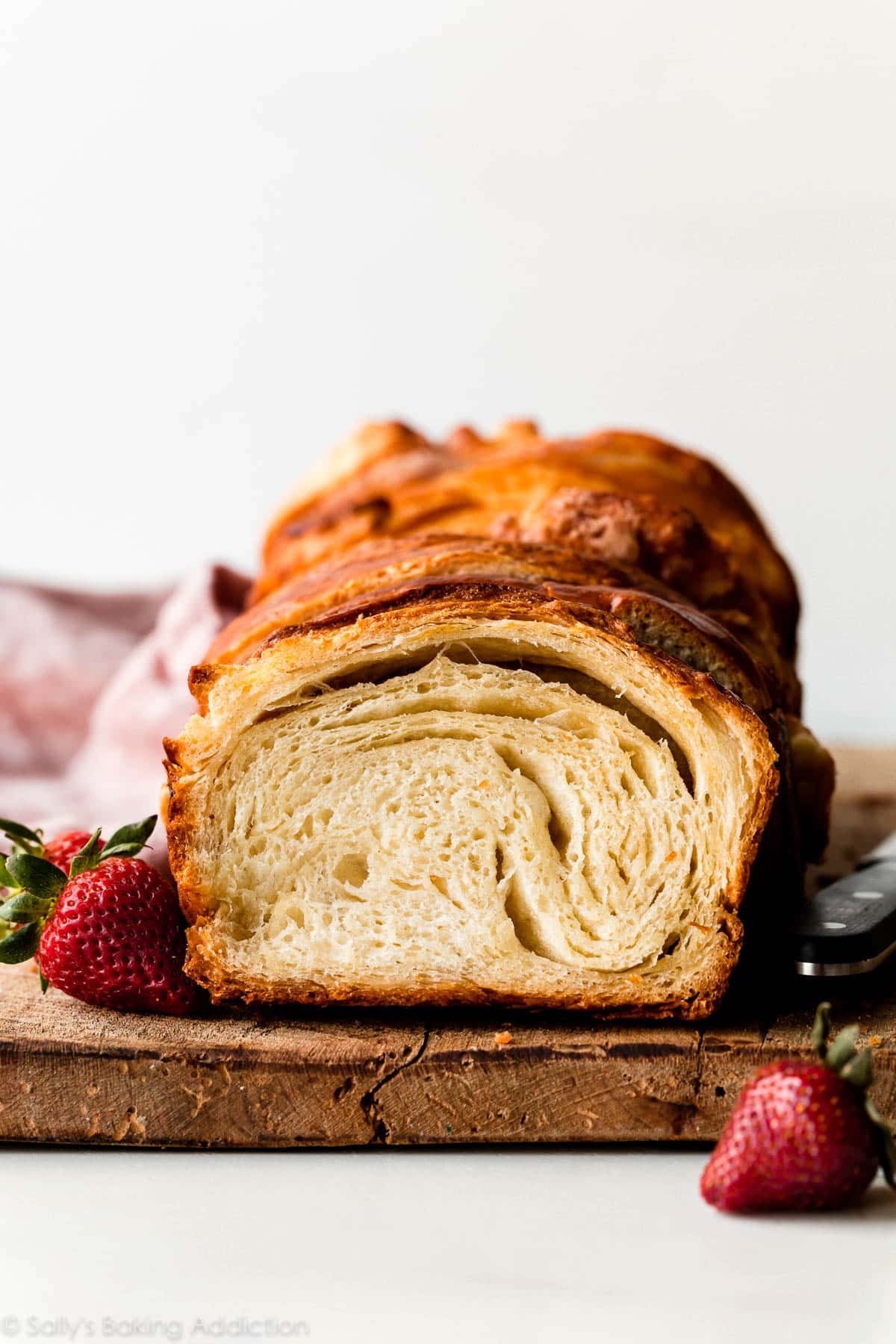 sliced croissant loaf on wooden cutting board with strawberries placed next to it