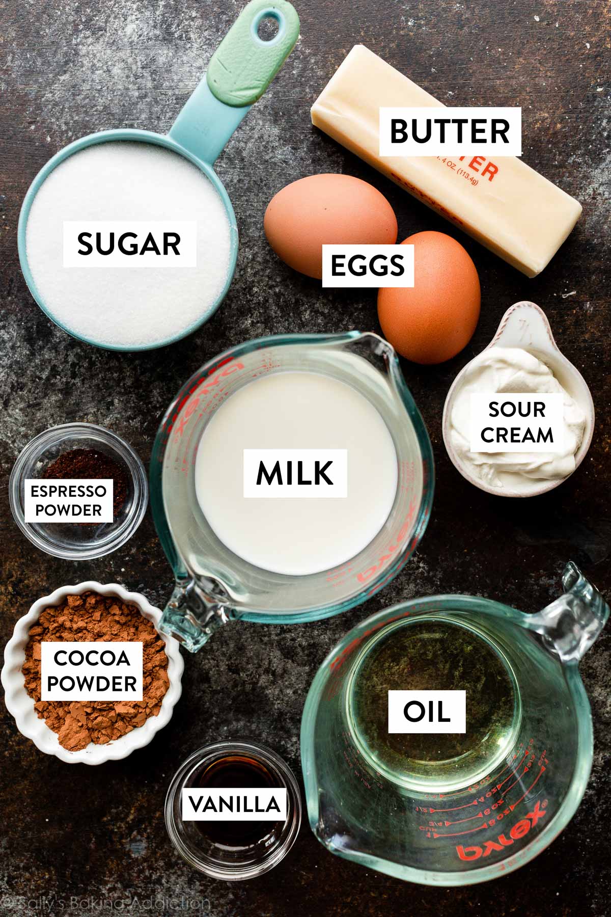 Zutaten auf einer schwarzen Arbeitsfläche, darunter Zucker, Butter, Eier, Milch, Öl und andere