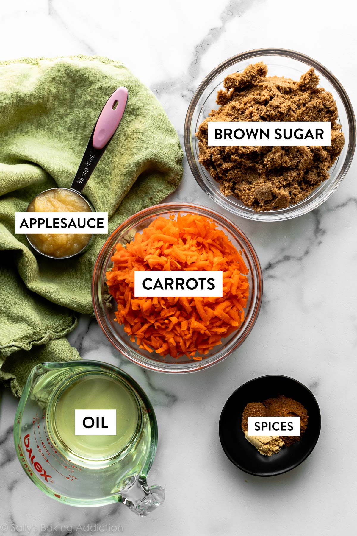 shredded carrots, brown sugar, spices, vegetable oil, and applesauce shown in bowls and measuring cups