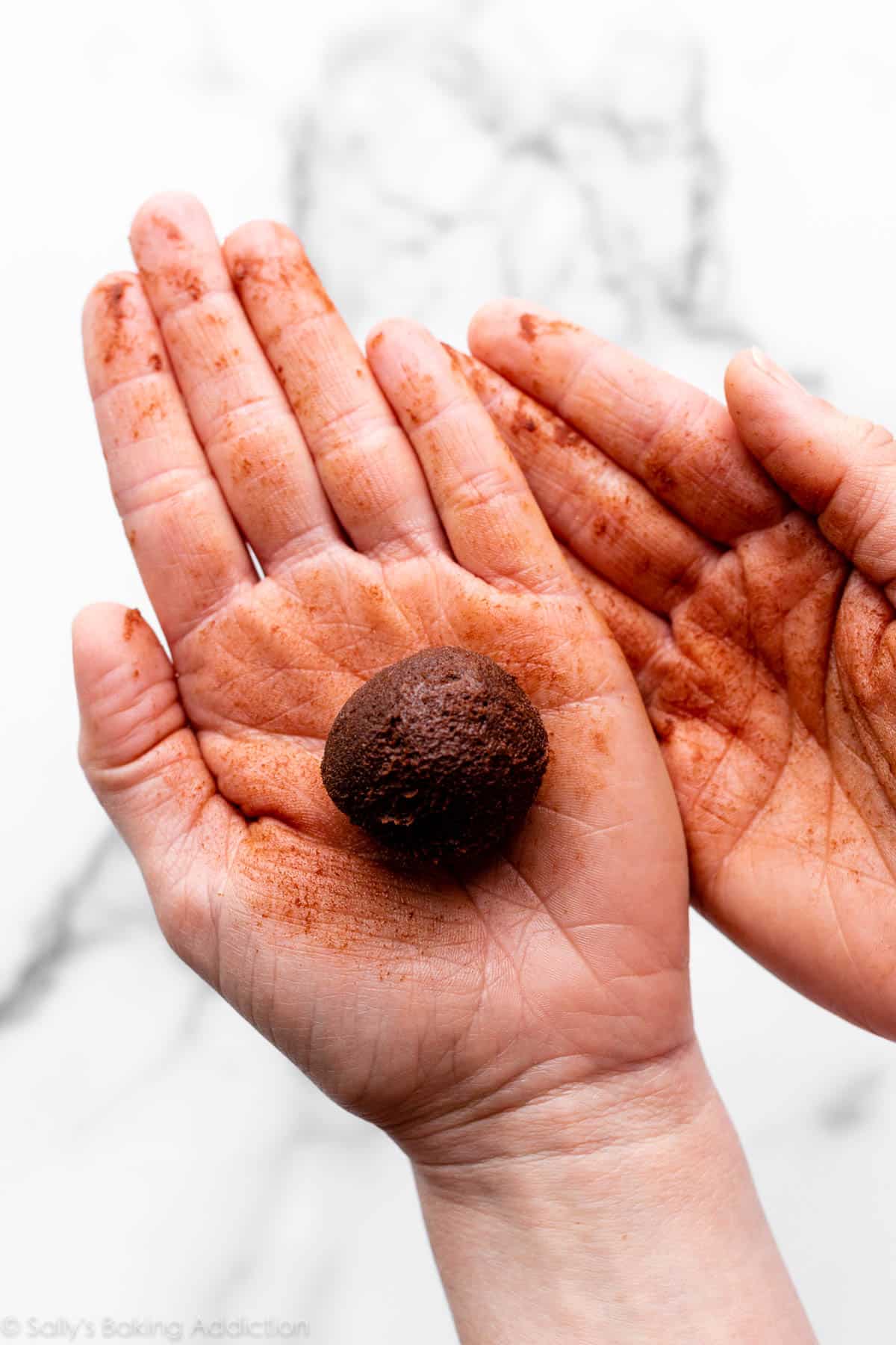 brownie dough ball in hands to display how messy the shaping can be
