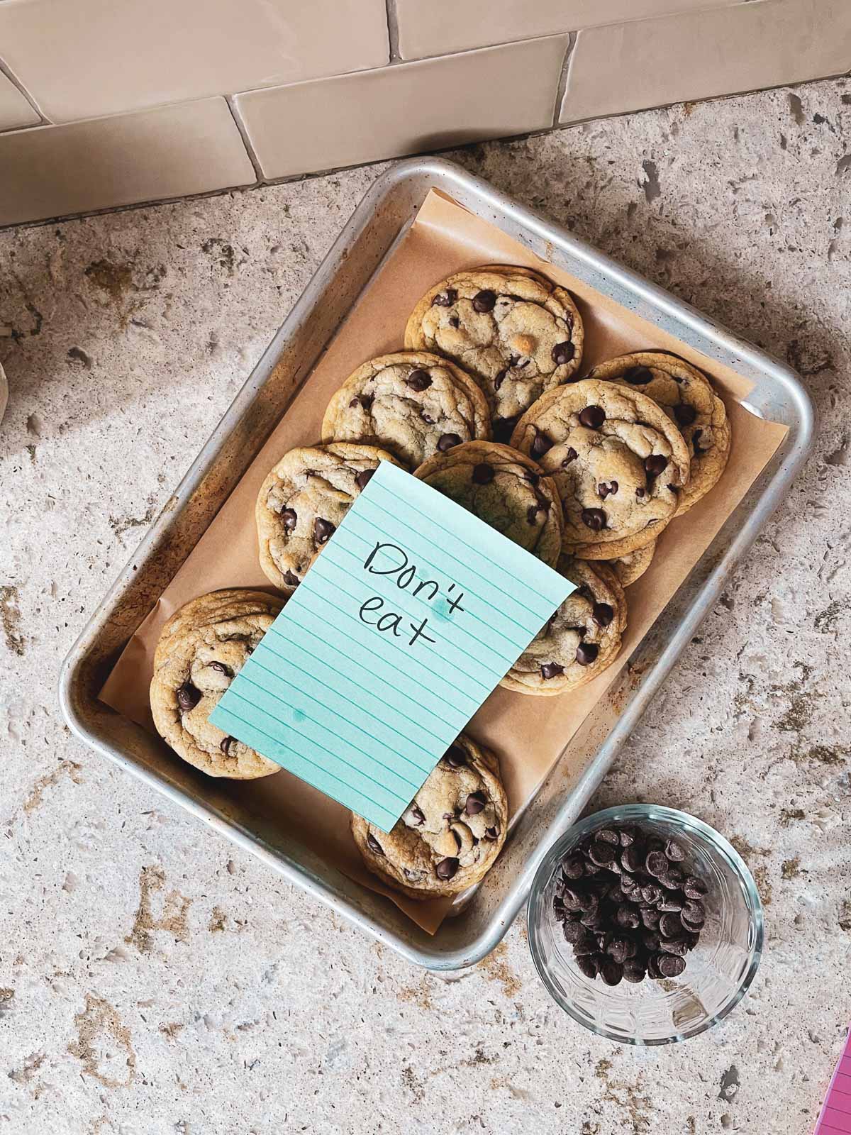 chocolate chip cookies on small baking sheet with "don't eat" note on top.