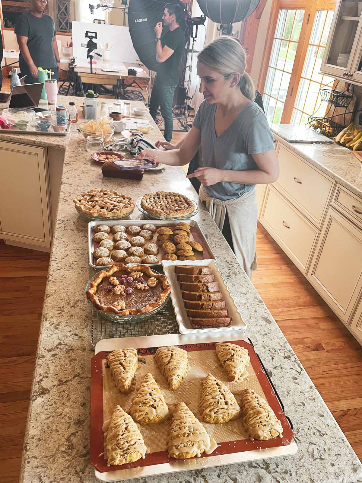 Sally with fall and holiday baked goods on counter including pumpkin pie, pumpkin bread, and cookies.