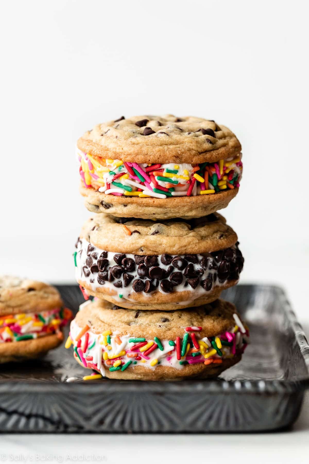 stack of chocolate chip cookie ice cream sandwiches with vanilla ice cream rolled in rainbow sprinkles and mini chocolate chips.