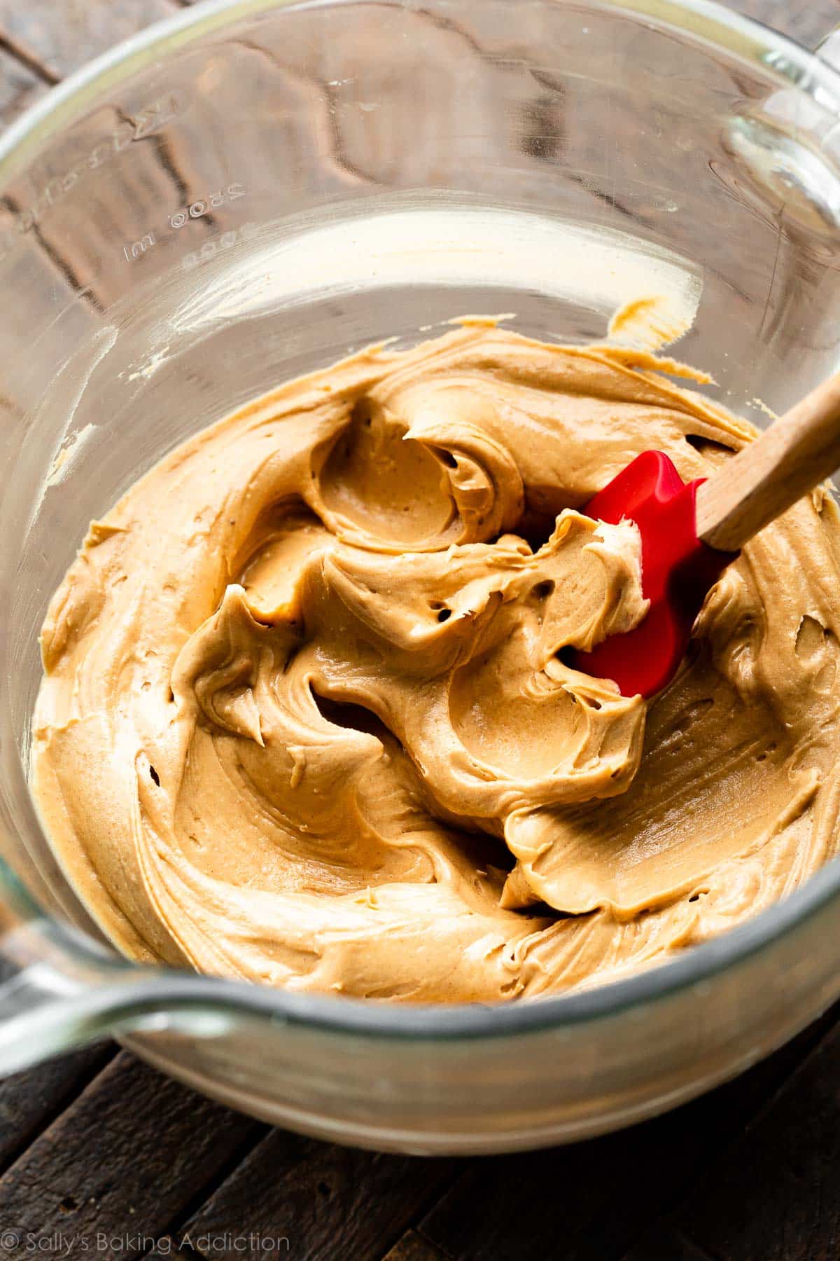 peanut butter frosting in glass bowl with red spatula.