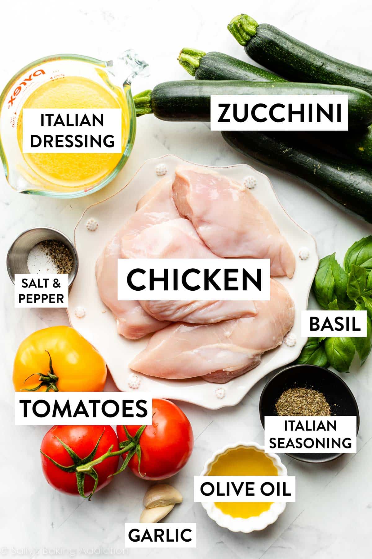 ingredients on counter including zucchini, basil, chicken on a plate, tomatoes, and 2 garlic cloves.